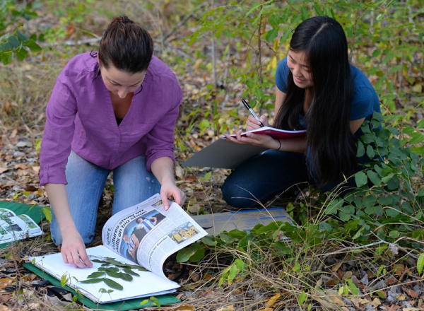 Two people looking at plants and a book.