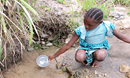 A young girl patiently collects water for her family from a slow-running spring. Collecting water from the source and treating it with chlorine tablets decreases the spread of cholera and other waterborne diseases. Photo: Courtesy of North Katanga UMC Health Board.